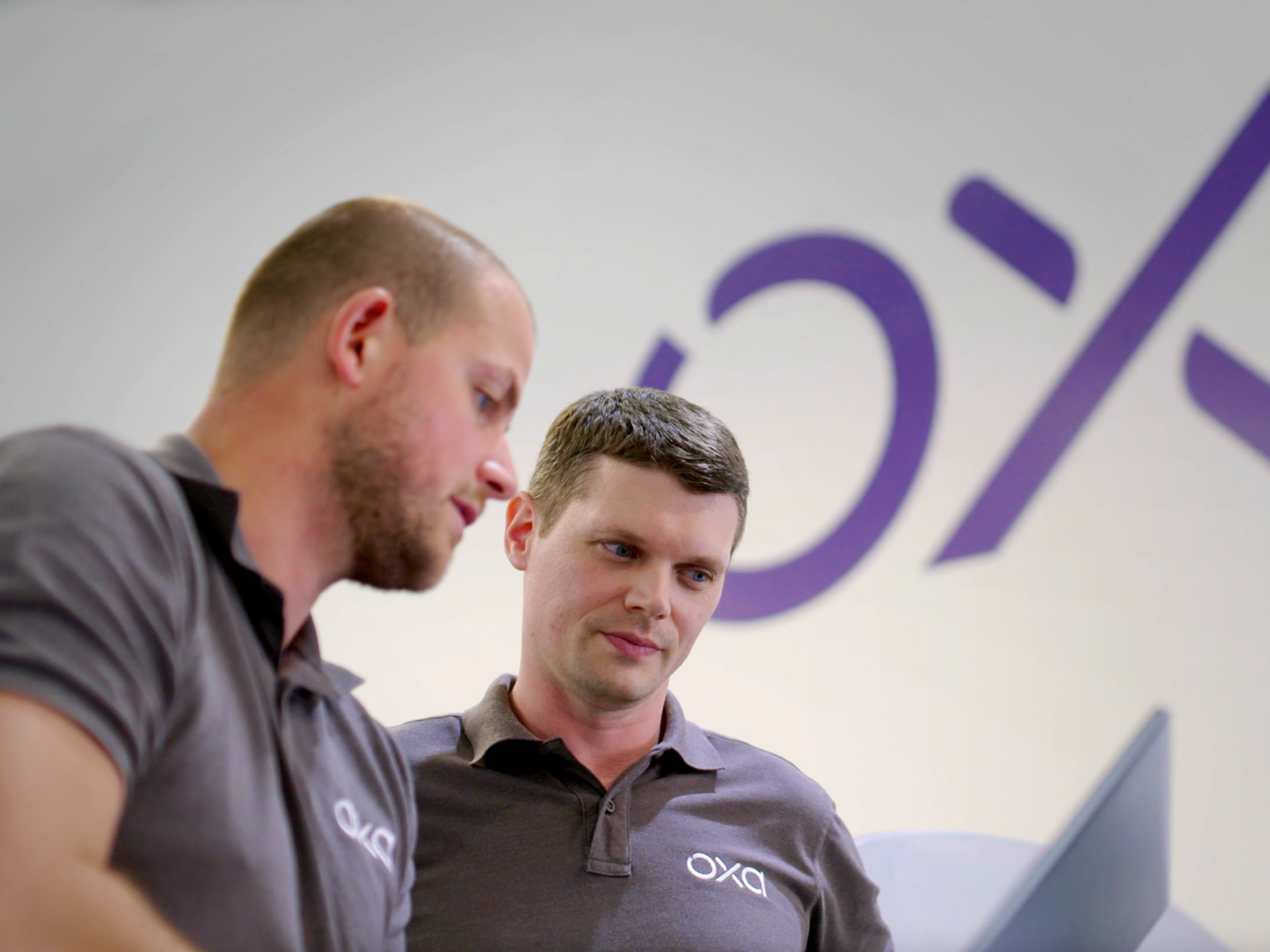 Oxa-engineers Oxa engineers reviewing software in front of Oxa branding.